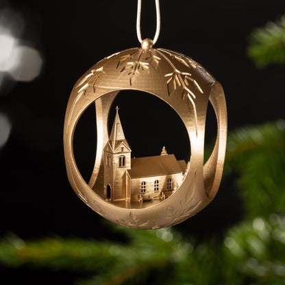 Auf dem Bild ist eine goldene Christbaumkugel zu sehen. Im Inneren der Kugel erhebt sich eine idyllische Kirche mit einem Kreuz, umgeben von Bäumen und einladenden Bänken. Diese friedliche Szenerie strahlt Ruhe und Geborgenheit aus.