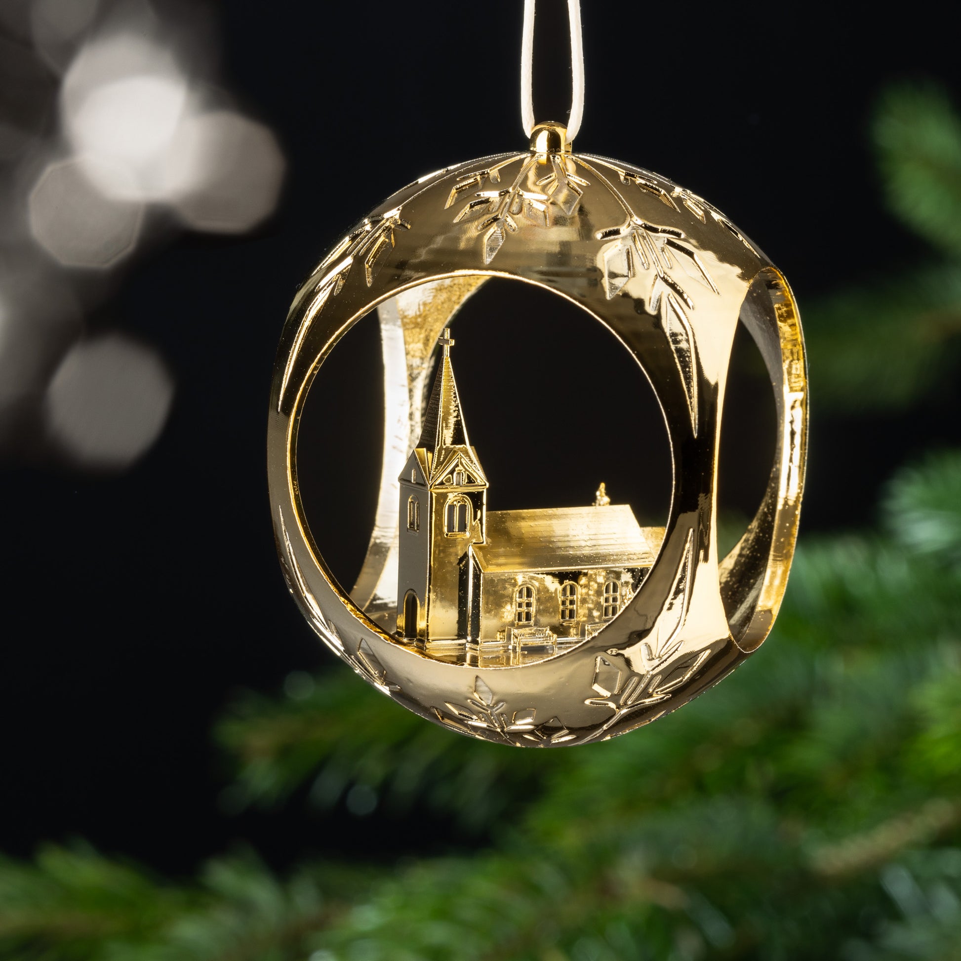 Auf dem Bild ist eine goldene Christbaumkugel zu sehen. Im Inneren der Kugel erhebt sich eine idyllische Kirche mit einem Kreuz, umgeben von Bäumen und einladenden Bänken. Diese friedliche Szenerie strahlt Ruhe und Geborgenheit aus.