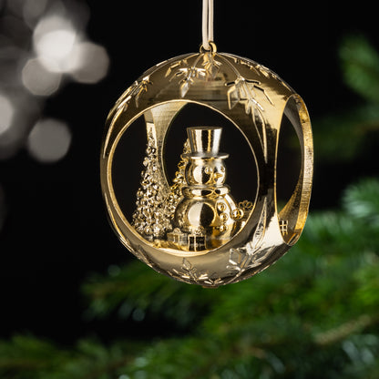 Auf dem Bild ist eine goldene Christbaumkugel zu sehen. Im Inneren der Kugel entdeckst du einen fröhlichen Schneemann, der zwischen Bäumen steht und von Geschenken umgeben ist. Diese verspielte Szenerie verbreitet Freude und Lebensfreude.