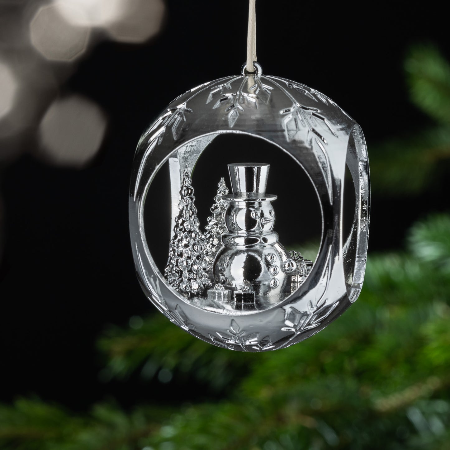 Auf dem Bild ist eine silberne Christbaumkugel zu sehen. Im Inneren der Kugel entdeckst du einen fröhlichen Schneemann, der zwischen Bäumen steht und von Geschenken umgeben ist. Diese verspielte Szenerie verbreitet Freude und Lebensfreude.